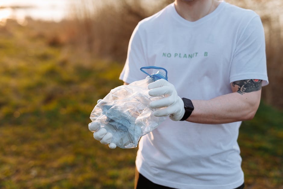 A person dressed in a white T-shirt with the text 'NO PLANT B' visible on the front, wearing white gloves and a black wristwatch, is holding a clear plastic bag filled with various discarded lightbulbs, including some with metallic bases and glass envelopes, in an outdoor setting with blurred natural background of grass and shrubs. The person is gripping the bag firmly with both hands, and the scene is illuminated by natural lighting, suggesting a daytime environment focused on waste collection or environmental cleanup activities. The image captures the act of handling potentially recyclable or hazardous waste materials, reflecting themes of responsible rubbish management and alternative waste disposal methods, consistent with services provided by companies like Rubbish Clearance Bromley.